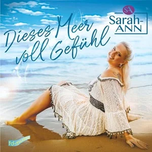 Dieses Meer voll Gefühl” von Sarah-ANN – Sängerin im weißen Kleid am Strand sitzend